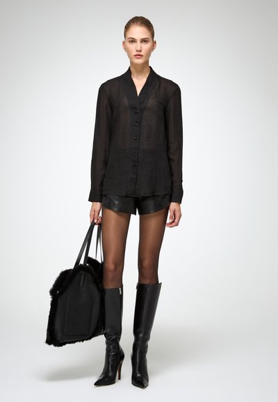 Camicia nera trasparente a maniche lunghe con chiusura a bottoni, abbinata a pantaloni corti in pelle nera, stivali neri fino al ginocchio e una borsa a tracolla nera con dettagli in pelliccia.