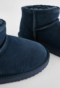 Marina mockask stövlar med mjukt foder av päls. Rundad tå, lågskuren design och kontrasterande sömmar. Gummisula för hållbarhet.