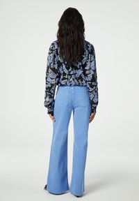 Schwarze Bluse mit floralem Muster, kombiniert mit hellblauen weiten Jeans. Die Bluse hat lange Ärmel, geraffte Bündchen und einen lässigen Schnitt.