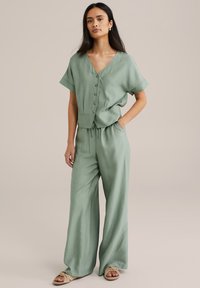Grön, texturerad tvådelad outfit bestående av en knappad blus med korta ärmar och löst sittande, vida byxor. Framträdande med dragsko i midjan.