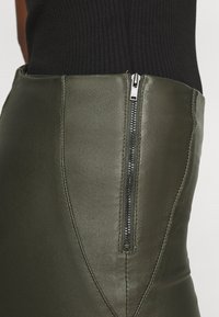 Falda de cuero verde oliva con cremallera lateral, que presenta un diseño ajustado y una textura suave. Las costuras crean una silueta estructurada.