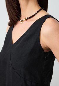 Schwarzes Leinenkleid mit V-Ausschnitt, ärmellosem Design und sichtbarem seitlichem Reißverschluss. Strukturierter Stoff mit glatter Oberfläche, figurbetonte Silhouette.