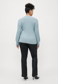 Lys blå strikket genser med bølgemønster, lange ermer og ribbestrikkede mansjetter, kombinert med svarte tettsittende bukser og svarte hælboots.