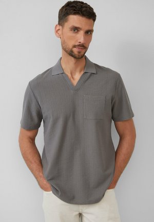Polo shirt gris à manches courtes avec un col en V et une poche frontale. Tissu texturé avec de subtiles rayures verticales. Coupe décontractée, design léger.