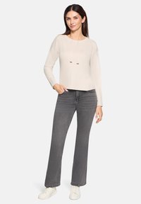 Beżowa bluzka z długim rękawem i okrągłym dekoltem, z detalem w postaci sznureczka, w połączeniu z szarymi spodniami dzwonami i białymi sneakersami.