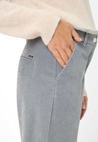 Grijze katoenen broek met een voorzakdetail en een klein zwart label. Slim fit en zachte textuur, gecombineerd met een licht crèmekleurige trui.