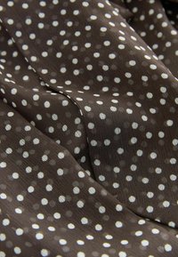 Pruun kangas sujuva tekstuuriga, millel on erineva suurusega valged polka punktid ühtlaselt üle pinna jaotatud, luues mustrilise kujunduse.