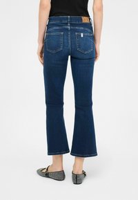 Jeans acampanados de color azul oscuro elaborados en denim, con una etiqueta en la cinturilla y dos bolsillos traseros. Combinados con unas bailarinas de estampado en blanco y negro.