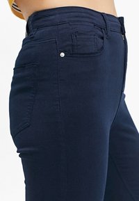 Jeans de tiro alto en azul marino con una textura suave, cinco bolsillos y un detalle de botón metálico en la parte frontal, presentando un diseño ajustado.