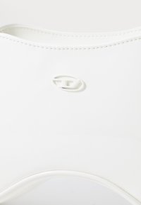 Sac en caoutchouc blanc avec une texture lisse, une forme légèrement courbée et un logo circulaire en relief bien visible au centre.