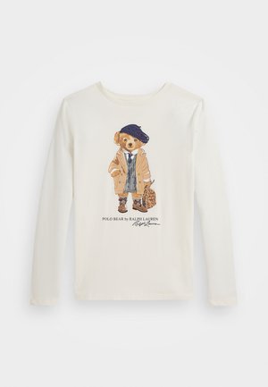Cream long-sleeve t-shirt featuring an illustration of a bear in a tan coat, blue beret, and patterned vest, with a leopard-print bag.