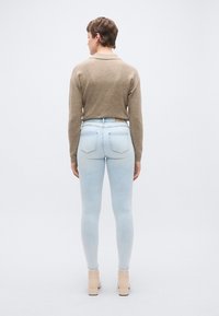 Φωτεινά γαλάζια στενά τζιν με ομαλή επιφάνεια, σε συνδυασμό με ένα εφαρμοστό μπεζ πουλόβερ. Το σύνολο χαρακτηρίζεται από μινιμαλιστικό σχεδιασμό και διακριτικές ραφές.