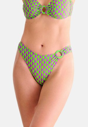 Femme portant un bikini à motifs verts et violets avec une ouverture en forme de clé à l'avant du haut et un détail d'anneau sur le bas taille haute, sur fond uni.