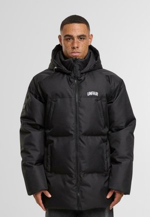 Giacca a vento nera con cappuccio, caratterizzata da un design trapuntato, zip frontale e due tasche laterali. Decorata con il logo "UNFAIR" sul petto.