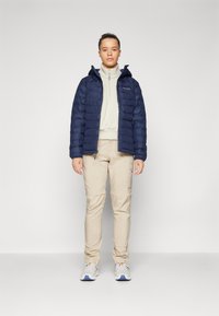Marineblå pustende jakke med hette, beige zip-up fleece, og beige cargo bukser; har teksturert stoff og en lett design.
