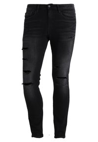 Vaqueros pitillo negros hechos de mezclilla, con varios parches desgastados. El diseño es ceñido al cuerpo con un estilo clásico de cinco bolsillos.