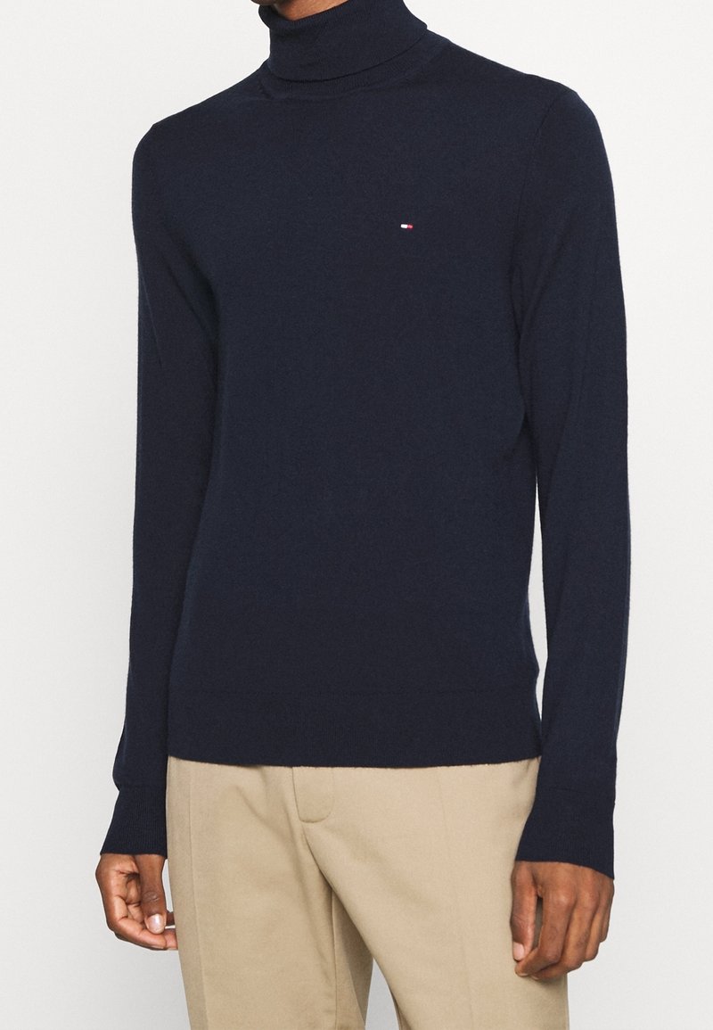 Suéter de cuello alto en navy con tejido de punto suave y mangas largas. Presenta un pequeño logo en el pecho y puños y dobladillo acanalados.