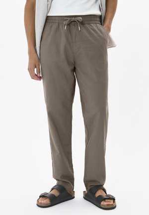 Brown linen pants with an elastic waistband and drawstring. Paired with black slides featuring a cork footbed and adjustable strap.