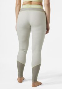 Leggings deportivos de color gris claro con una tela texturizada, que presentan un panel marrón en contraste y costuras amarillas en la parte inferior.