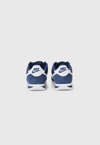 Ténis Nike com um esquema de cores azul-marinho e branco, materiais em camurça e malha, forma arredondada e logótipo proeminente no calcanhar.