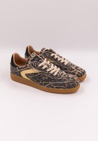 Un paio di sneaker basse con tessuto a stampa leopardata, lacci color beige, dettagli dorati sui lati, linguette nere sul tallone e suole in gomma color caramello su uno sfondo chiaro.