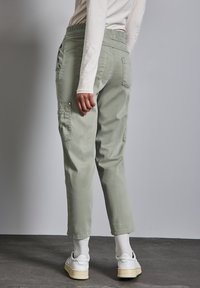 Helle grüne Cargo-Hose mit schmaler Passform, elastischem Bund und seitlichen Taschen. Getragen mit weißen Turnschuhen und strukturierten weißen Socken.