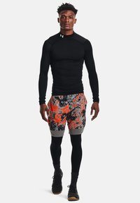 Haut de sport noir à manches longues associé à un short multicolore avec des motifs abstraits orange, gris et noir. Porté avec des chaussettes et des chaussures noires.