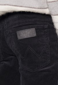 Svarta manchesterbyxor med en läderetikett från Wrangler på bakfickan och kontrasterande sömmar i ett zickzackmönster.