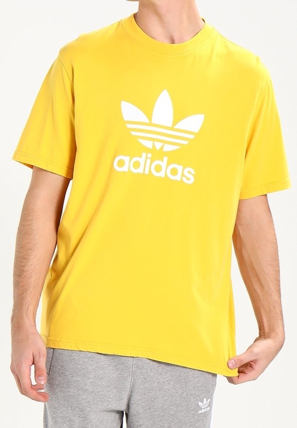 Žluté bavlněné tričko s velkým bílým logem Adidas a designem tří pruhů na přední straně. Volný střih s kulatým výstřihem.