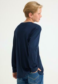 Langarm t-shirt van navyblauw katoen met ribbeltextuur, ronde halslijn en een ontspannen pasvorm. G gedragen met lichtblauwe denim jeans.