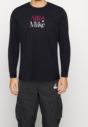Black long-sleeve shirt with "AIR Mike" text in pink and white, featuring a pink jump man logo. Worn with black cargo pants.