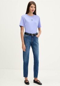 Světlofialové tričko s malým černým logem, doplněné o modré džíny s vysokým pasem, upevněné černým pásem a černé baletní baleríny.