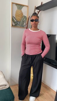 Red and white striped long-sleeve shirt paired with loose black trousers and white sneakers, showcasing a casual look with simple accents.