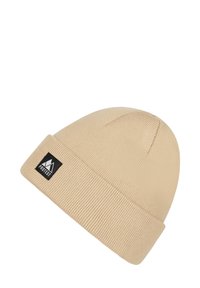 Beige knit beanie with a folded cuff, featuring a black rectangular logo tag with mountain graphics. Made of soft, textured fabric.