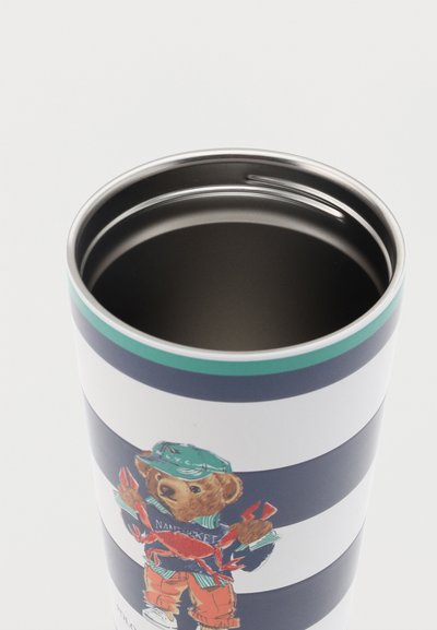 Ριγέ ποτήρι με μια αρκούδα παιχνιδιών που φοράει πράσινο καπέλο και κρατάει έναν κόκκινο κάβουρα, γεμάτο με σκοτεινό υγρό.