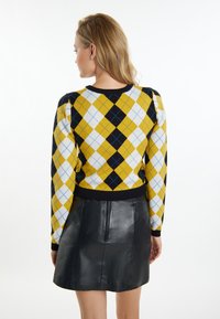 Maglione argyle giallo e nero con dettagli blu, dotato di maniche lunghe e orlo a costine nero, abbinato a una gonna in pelle nera.