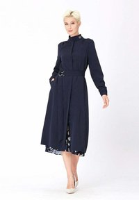 Robe longue à manches longues de couleur marine avec un col haut, une ceinture à la taille et des poches latérales ; elle présente un ourlet plissé et une doublure intérieure à motifs.