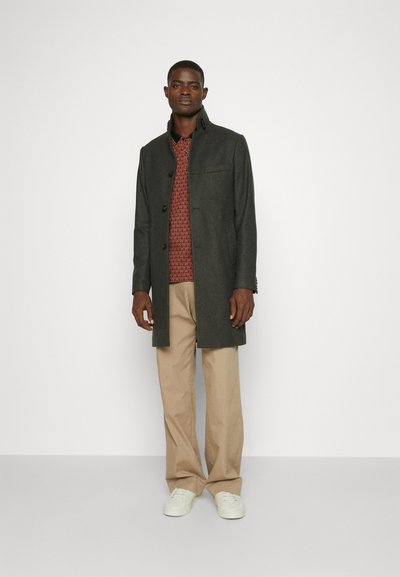 Gray wool coat with a high collar and front buttons, worn over a red patterned shirt, beige trousers, and white sneakers.