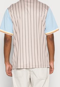 Maglietta a maniche corte beige in jersey con strisce verticali nere, maniche azzurro chiaro e strisce di accento arancione e giallo ai polsini.