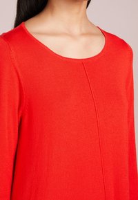 Maglione rosso lavorato a maglia con scollo rotondo e dettagli cuciti sottili, caratterizzato da una texture morbida e una silhouette aderente.