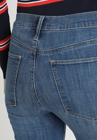 Mörkblå denimjeans med en figurnära design, två bakfickor och synliga sömnadsdetaljer. Tyget har en lätt struktur.