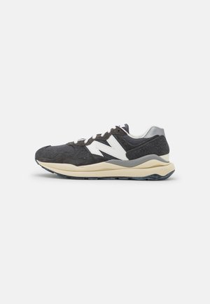 Niedriger schwarz-weißer Sneaker mit Wildleder- und Mesh-Einsätzen, Schnürverschluss, dicker beiger Sohle und großem weißem "N" Logo an der Seite.