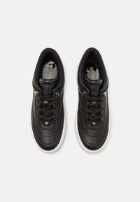 Mustade nahast spordijalatsid, millel on tikandiga disain, valge kummist tallaga, ümar nina ja mustad paelad. Külgedel on kuldsed aktsendid.