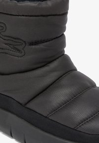 Černá nadýchaná bota s prošívanou texturou, s textilním svrškem a gumovou podrážkou. Jednoduchý design s minimálním brandingem a detaily prošívání.