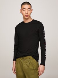 Fekete, hosszú ujjú póló kerek nyakkivágással, melyen a jobb ujján "TOMMY HILFIGER" felirat található, valamint kisebb logó a mellkason.