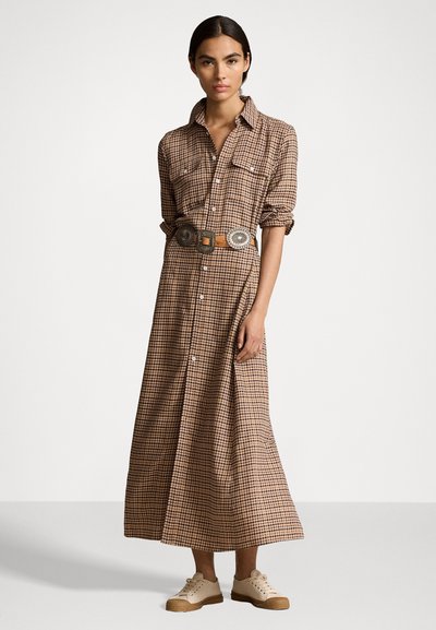 Μακρύ καρό φόρεμα σε καφέ και κρέμα αποχρώσεις, με κουμπιά μπροστά, ρεγκλάν μανίκια, τσέπες στο στήθος και διακοσμητική ζώνη, συνδυασμένο με ανοιχτόχρωμα αθλητικά παπούτσια.