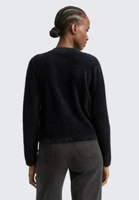 Schwarzer, flauschiger Pullover aus weichem Material, mit langen Ärmeln und lockerer Passform, kombiniert mit schwarzen Jeans.