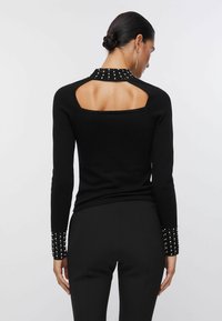 Haut noir à manches longues avec un dos ouvert et des accents cloutés aux poignets. Confectionné dans un tissu lisse avec une coupe ajustée.