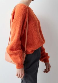Suéter naranja suave con un escote ancho y corte holgado, combinado con pantalones grises y un pequeño bolso de hombro rosa. Mangas largas, ligeramente enrolladas.