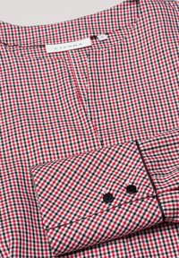 Camicia a quadri rossi e neri con polsino abbottonato, caratterizzata da un colletto a discesa e una piccola sottomanica. Il materiale è liscio, con un design strutturato.